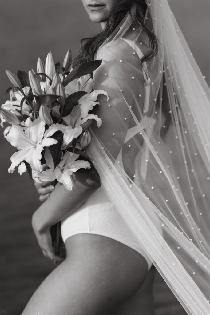 bride in bathing suit holding lilies Black and white wedding photographer and cinematographer