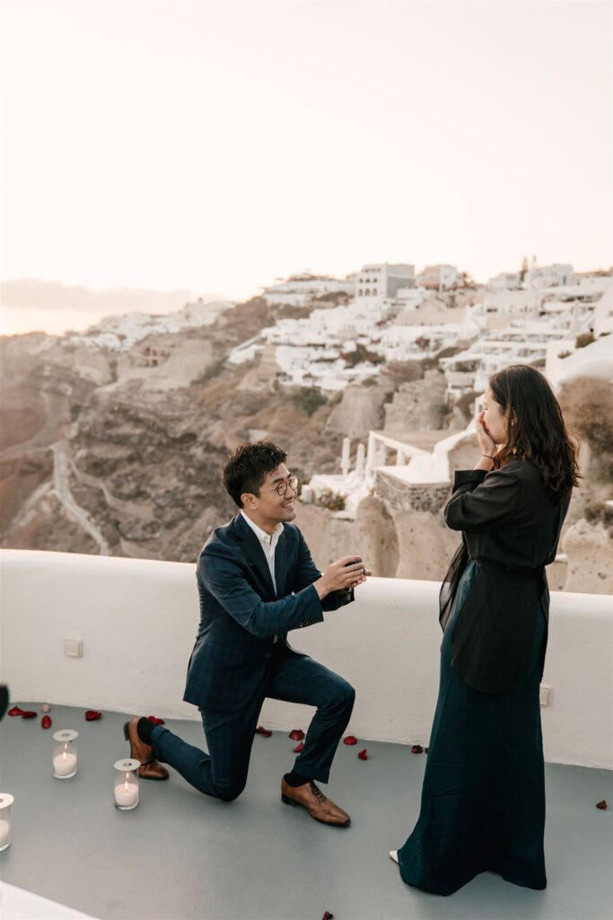 he is on the knee in Santorini an a terace at sunset